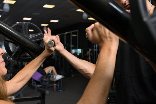 Personal trainer correcting a woman's grip on a gym machine handle, close-up of hands showing proper technique and safe workout guidance