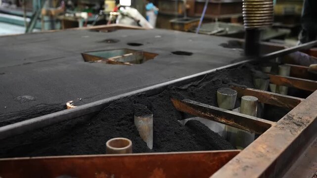 Foundry worker smoothing black moulding sand inside a steel flask by hand while preparing a large mould for metal casting