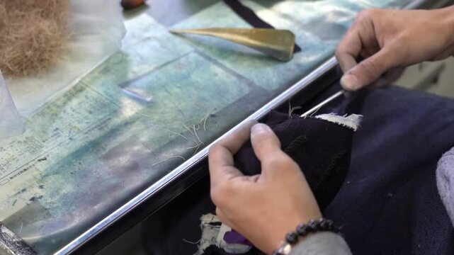 Craftswoman trims stitched indigo fabric with scissors beside a tuft of raw wool on a glass topped table