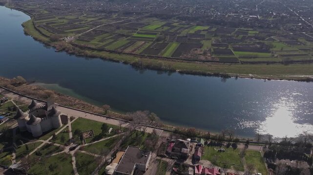 Wide drone panorama backwards over Soroca, Moldova, showing dense residential neighborhoods beside the winding Dniester River and the surrounding rural landscape.