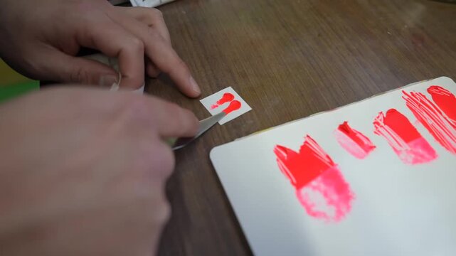 Technician comparing a small red paint sample against a card of reference swatches on a workshop table