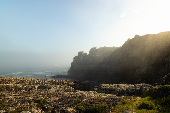rock formations in fog filtering through late afternoon sunlight, Hermanus, South Africa