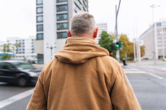 Man walking in a city in a brown hoodie while crossing the street