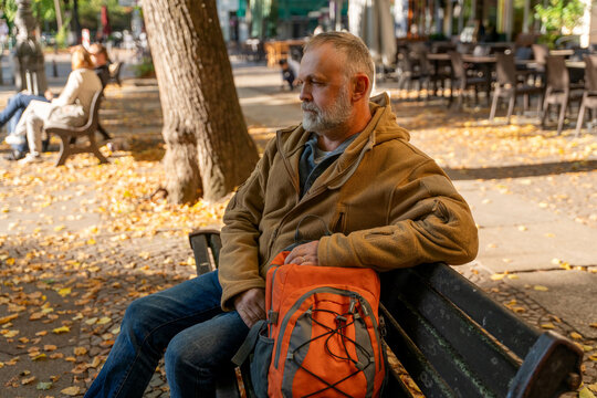 Man sitting on a park bench with an orange backpack during autumn