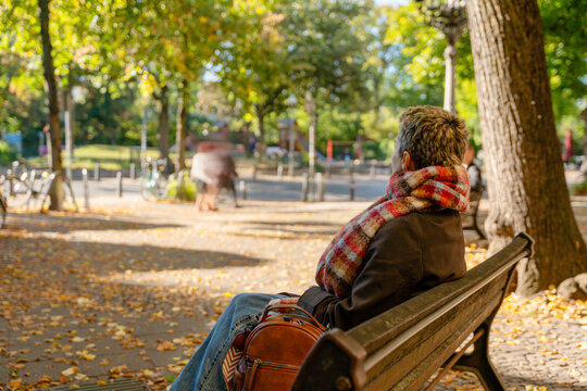Person sitting on bench in park enjoying autumn scenery with leaves