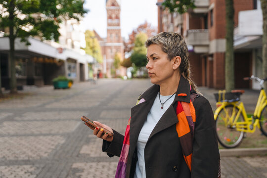 Woman holding a phone while standing in an empty street with