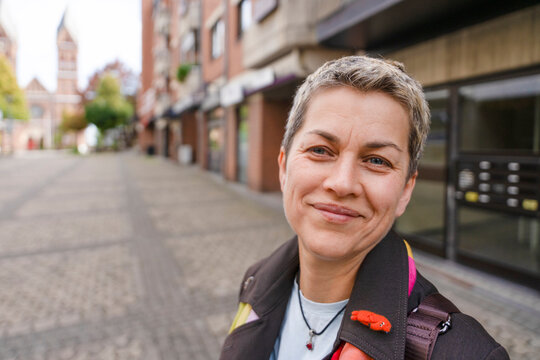 Woman smiles on a cobblestone street in a city with buildings and
