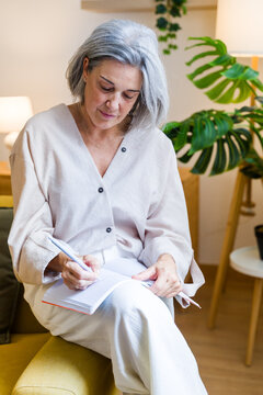 White woman writing in a notebook in living room with plants