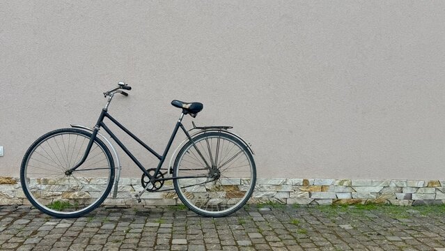 Old Vintage Bicycle Leaning Against Plain Light Stone Wall, Abandoned Retro Bike. Lonely Classic Bicycle Parked by Light Textured Stone Wall with Copy Space