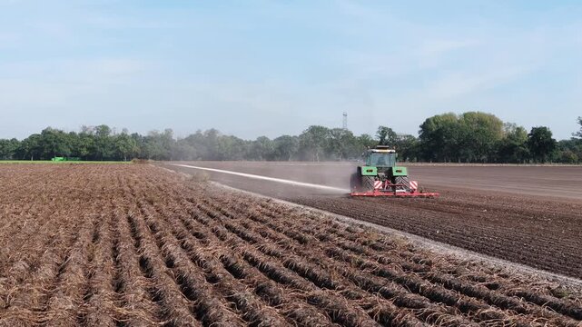 Green tractor plowing a large field on a sunny dry day in the flat Dutch countryside, showcasing agricultural work, farming and rural landscape in the Netherlands