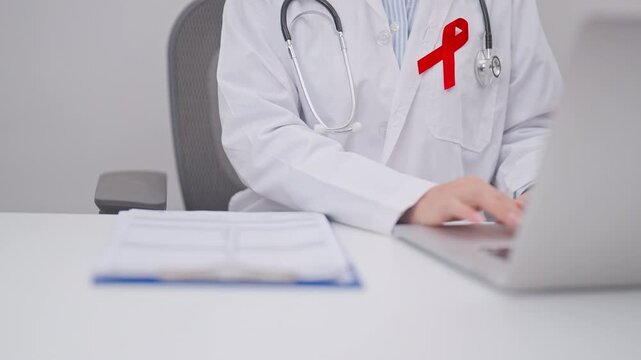 doctor using laptop and report notes on notebook. red ribbon concept of December World Aids Day, MADD, October Red ribbon week, February Heart month, Marfan Syndrome, May Stroke awareness
