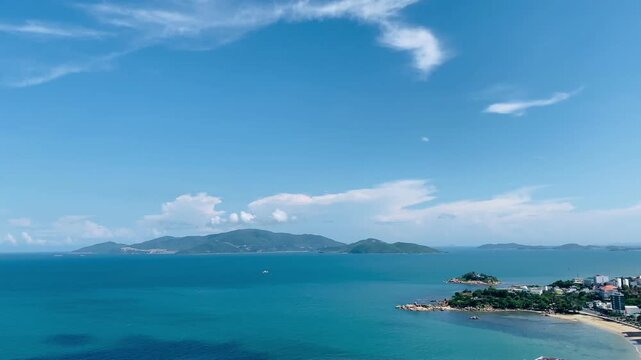High-angle panoramic view of the beautiful blue sea bay in Nha Trang, Vietnam, featuring lush green islands, a sunny sky with soft clouds, and the coastline.