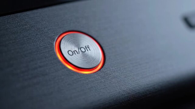 Close up of finger pressing round on off button as orange indicator illuminates on dark textured electronic device, showing activation in a modern technology detail