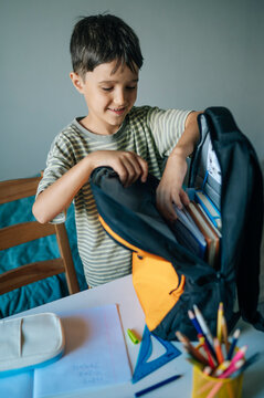 Smiling boy packs his backpack with books for school indoors