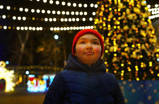 A girl admires a decorated Christmas tree outdoors at night