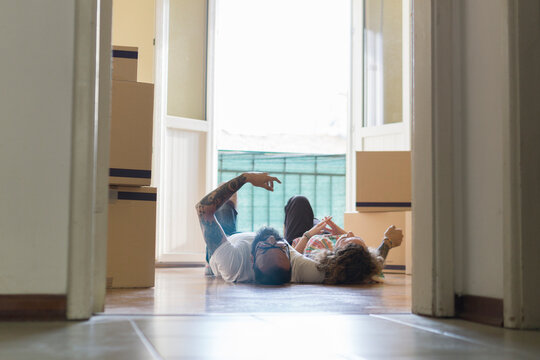 Couple lying side by side on the floor of new home in front of open balcony door