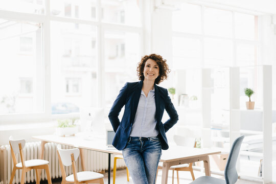 Businesswoman in office sitting on desk, looking confident