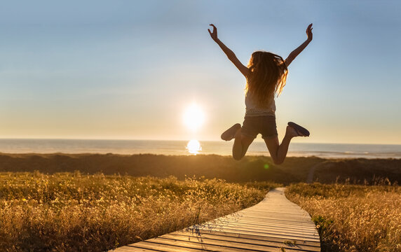Young woman jumping on boardwalk at the beach with raised arms