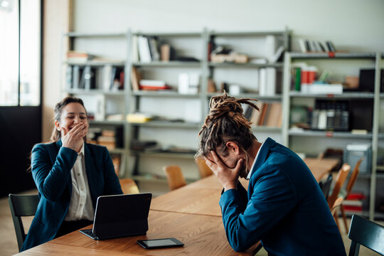 Woman laughs at exhausted man with dreadlocks in the office