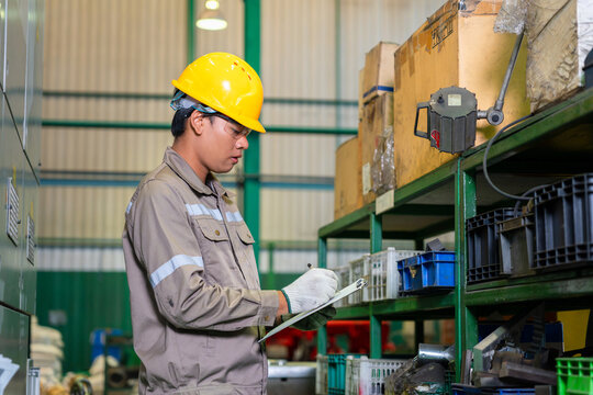 Warehouse worker holding checklist and inspection stock in manufacturing facility, technician checking inventory and quality control in workshop, factory worker writing on clipboard in warehouse plant