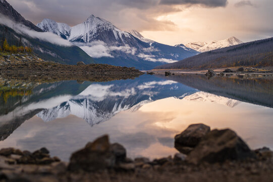 Serene lake reflection captures peaceful mountain wilderness landscape scenery at sunset in Canada under dramatic snow peak sky