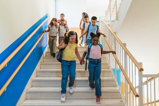 Group of happy elementary school children with backpacks descending stairs, fostering friendship and learning in education