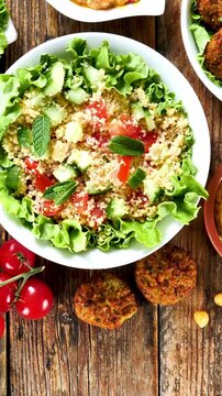 assortment of lebanese food featuring tabbouleh salad,  falafel, hummus and fresh tomatoes on wooden table top view