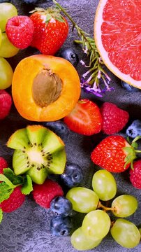 Sliding camera view over fresh berries, kiwi, apricot, grapes, mango, grapefruit on slate background