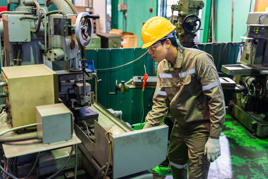 Asian factory worker operating heavy machinery and milling machine tool in workshop, professional industrial technician wearing safety helmet working in manufacturing plant