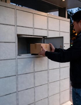 Man placing a cardboard parcel into a delivery locker