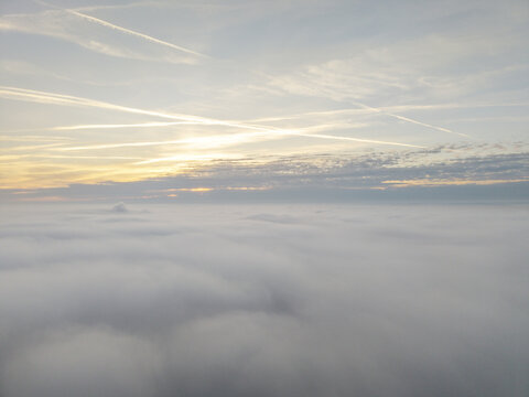 Aerial view of a thick layer of clouds at sunset with contrails streaking across the sky above Krakow, Lesser Poland Voivodeship, Poland.