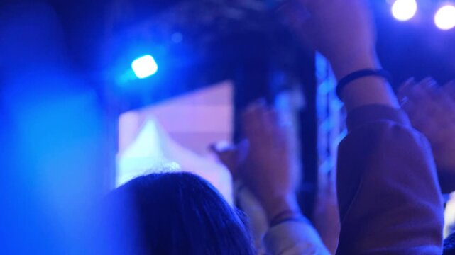 View from behind showing only raised hands of music fans swaying in sync at a nighttime live performance, a spectacular free concert for everyone, music events, collective celebration