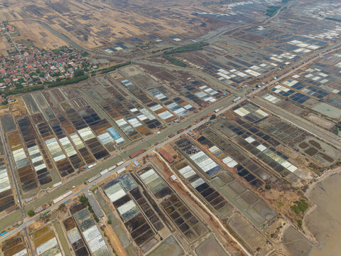 Aerial view of the Salt Ponds, featuring a grid of rectangular evaporation pans with varying water levels, situated near a coastal road in Kedung, Central Java, Indonesia.