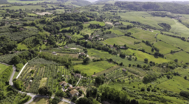 Aerial view of Tuscany rolling hills featuring lush green fields, olive groves, scattered farmhouses, and winding country roads in Montepulciano, Italy.