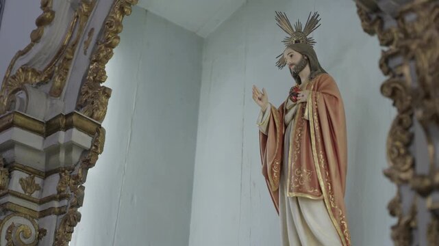 A statue of the Sacred Heart of Jesus with a gold halo, framed by gilded baroque carving inside a white chapel niche.