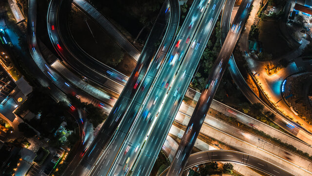 Aerial view of a complex highway interchange at night with illuminated light trails from moving vehicles in Jakarta, Indonesia.