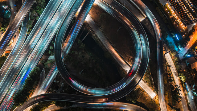 Aerial view of a complex highway interchange at night with vibrant light trails from moving vehicles illuminating the urban infrastructure in Jakarta, Indonesia.
