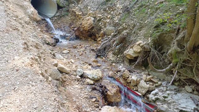 Water flowing from a concrete drainage pipe culvert under a rural gravel road

