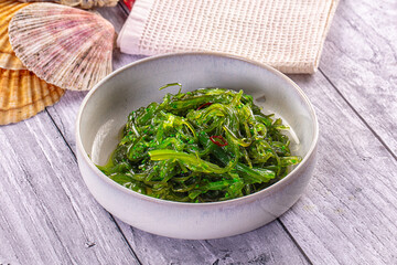 Wooden table with grey ceramic bowl containing green seasoned seaweed salad, Asian side dish © Andrei Starostin