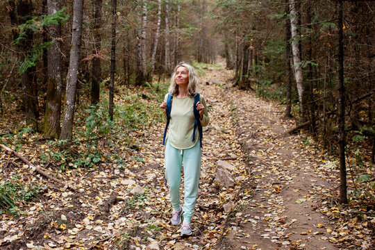 Middle aged woman hiking a forest trail during a digital detox. Nature walk and mindful outdoor break. Screen free lifestyle, personal wellbeing and unplugged living.