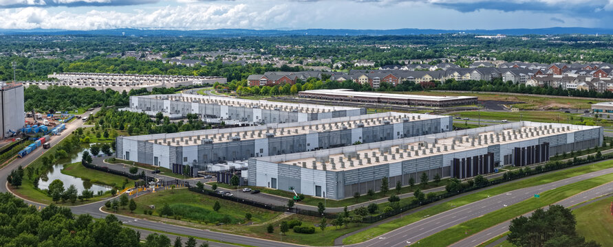 Aerial view of a large data center complex with multiple industrial buildings, cooling units on rooftops, and surrounding green spaces in Ashburn, Virginia, United States.