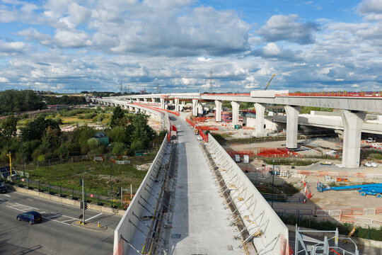 Aerial view of high speed rail construction featuring concrete viaduct pillars and ongoing infrastructure development in a rural landscape under a cloudy blue sky in the United Kingdom.