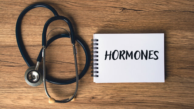 Hormones text written on spiral notebook placed beside medical stethoscope on wooden background