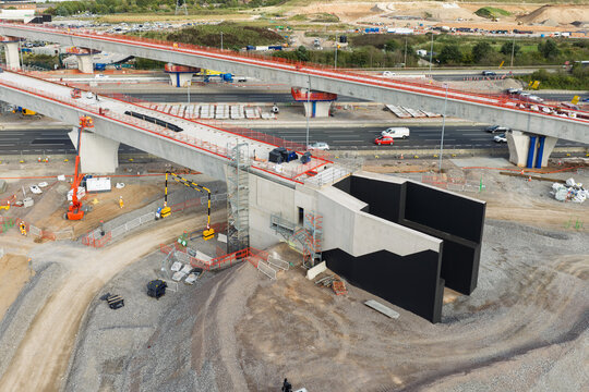 Aerial view of high speed rail construction featuring concrete viaducts, support pillars, and heavy machinery near a highway in the United Kingdom.