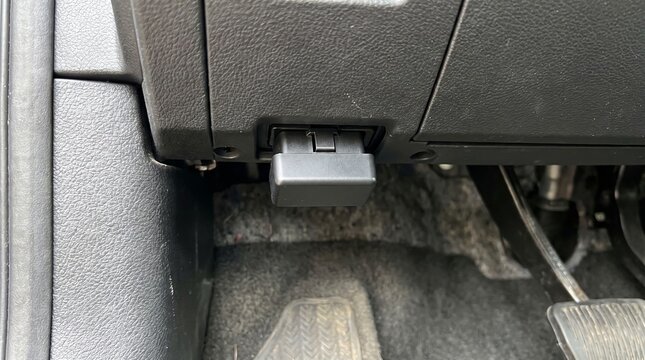 Keyless Car Theft Concept, Black Dongle Plugged into a Car OBD Port Under the Dashboard