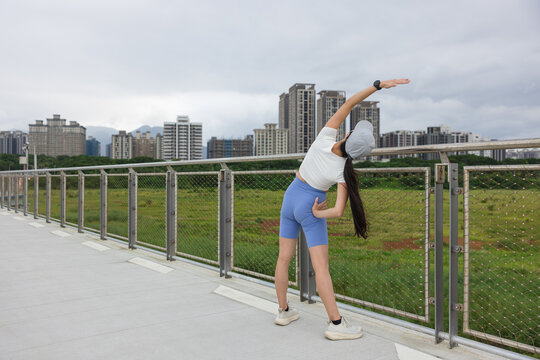 Asian woman doing side body stretch on bridge near city