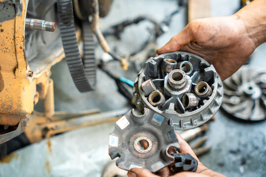 Mechanic holding a motorcycle CVT variator pulley with roller weights during transmission repair in a workshop.