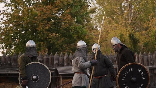 Viking warriors in full armor practicing combat drills with shields outdoors.