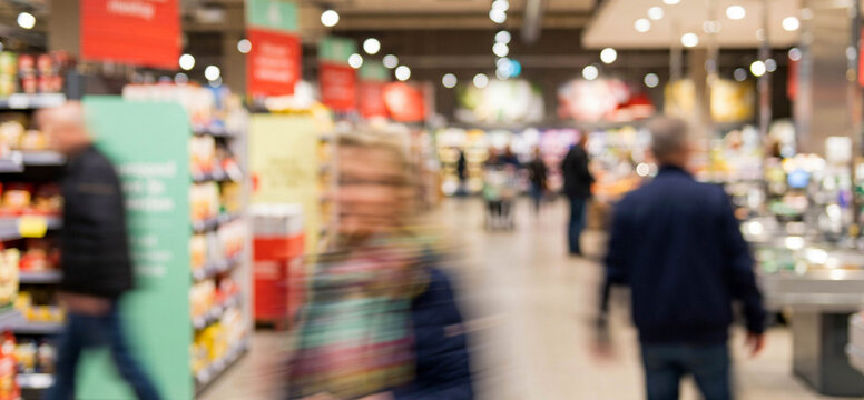 A bustling supermarket scene with shoppers moving through blurred aisles, showcasing a lively retail environment full of products, signage, and ambient lighting.