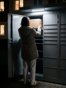 Woman in pajamas retrieving parcel from locker at night